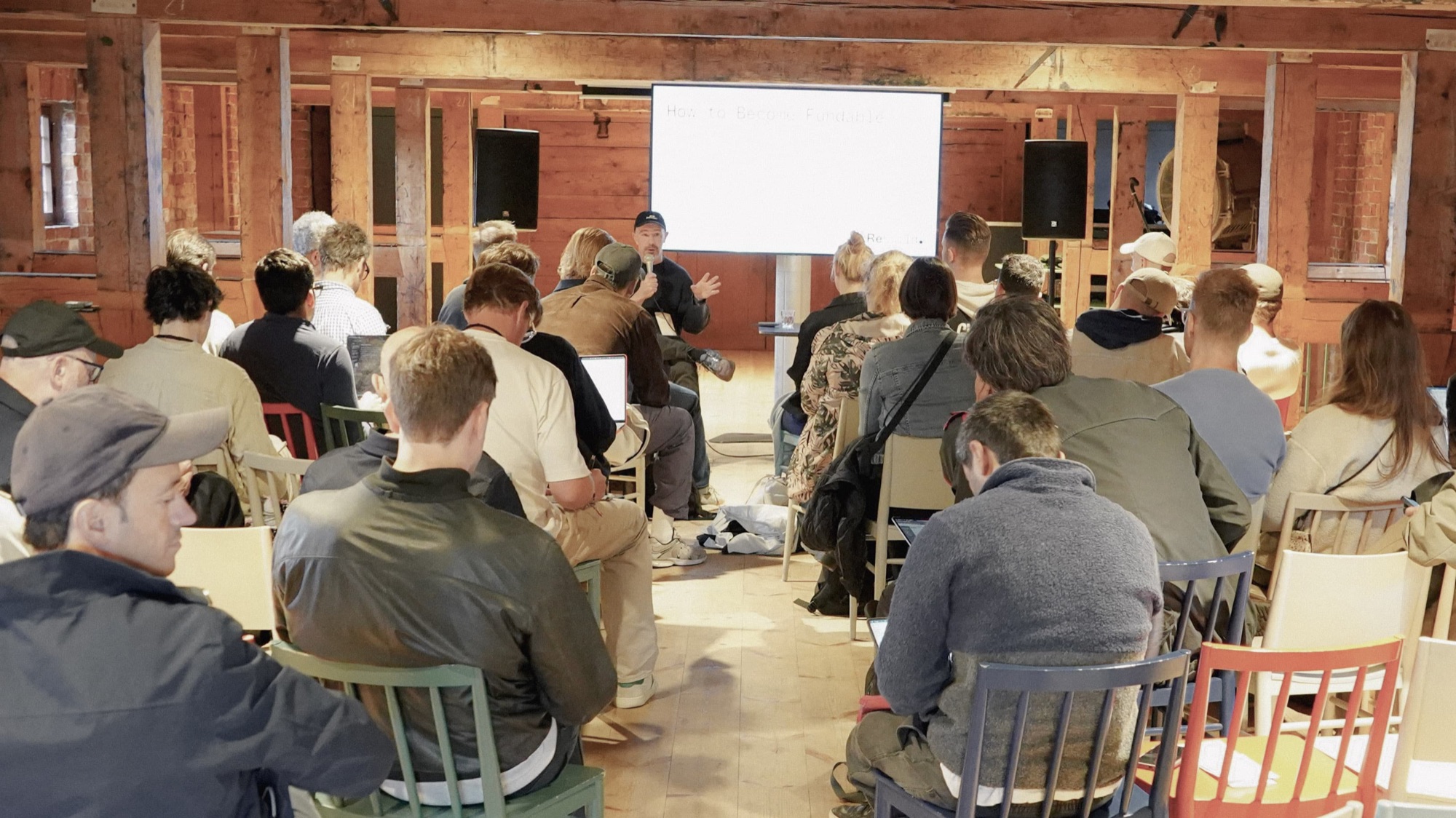 Attendees seated in a timber-walled hall listen to the “How to Become Fundable” session at Rebuild2.