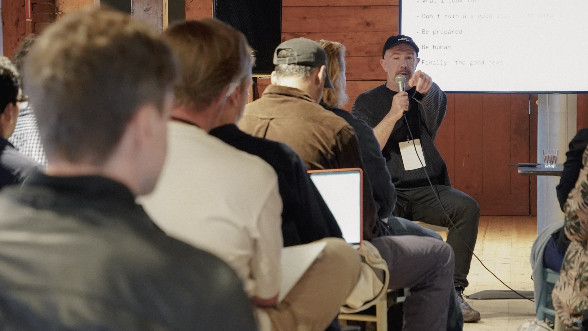 The speaker addresses the room with a microphone, in front of a slide listing points such as “Don’t ruin a good story with data” and “Be human”.