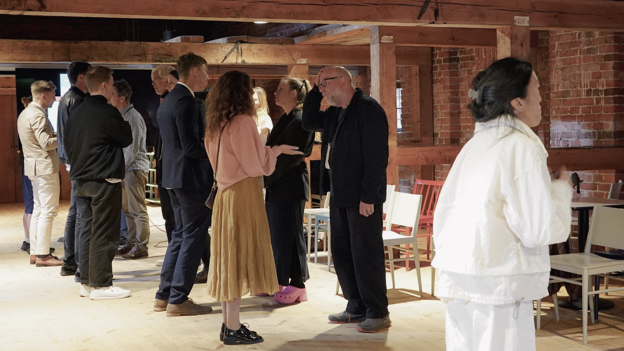 Attendees stand and talk in small groups in a timber-beamed hall with exposed brick walls.