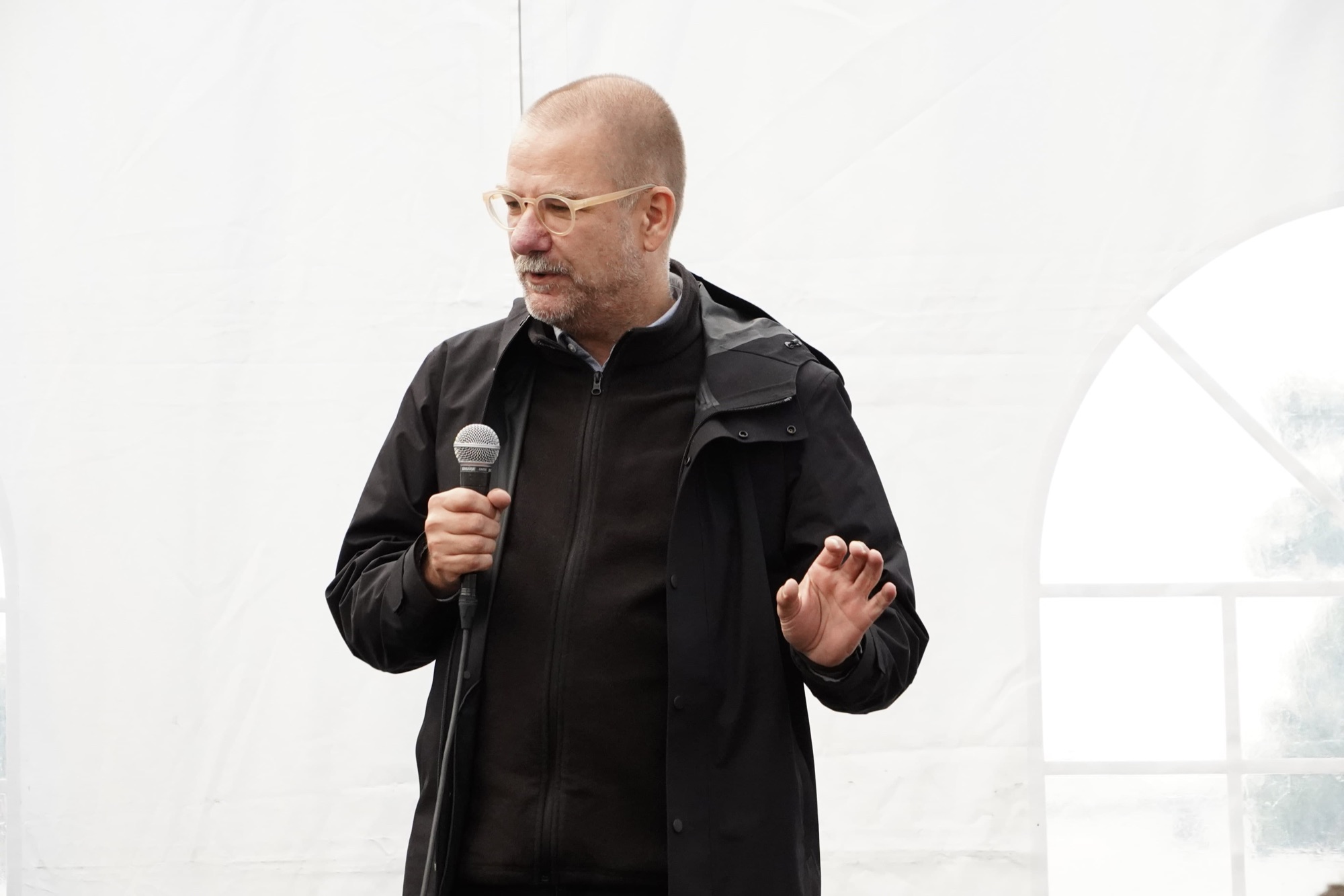 A Social Design Framework track leader in glasses gestures while speaking into a microphone.